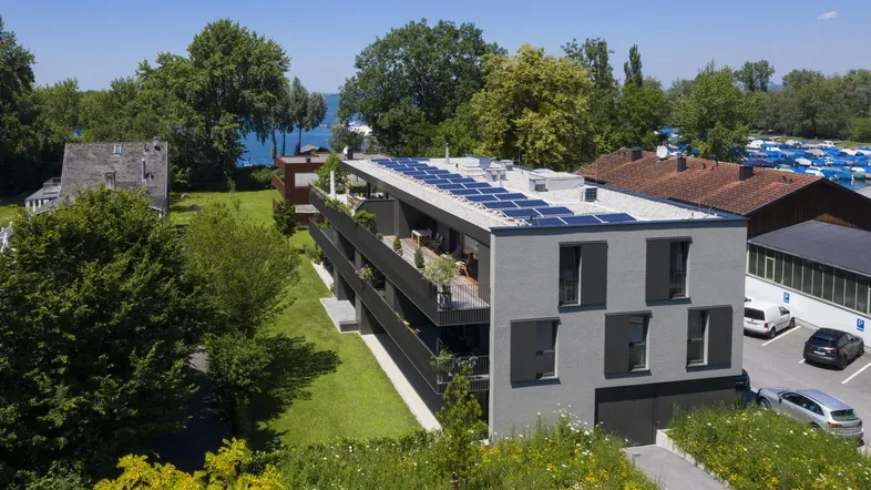 Moderne Wohnanlage mit Solarpaneelen auf dem Dach, Balkonen und Blick auf den See.