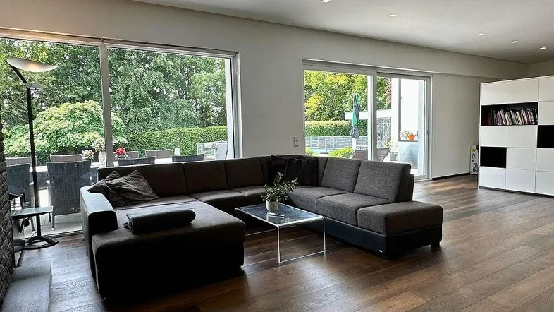 Geräumiges Wohnzimmer mit großen Fenstern, die einen Blick auf den Garten und die Terrasse bieten.