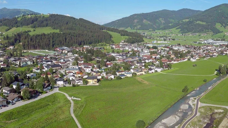 Luftaufnahme einer malerischen Stadt in einem Tal, umgeben von grünen Hügeln und Bergen mit einem Fluss.