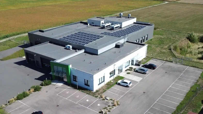 Moderne Gewerbeimmobilie mit Photovoltaikanlage auf dem Dach und großem Parkplatz, umgeben von Feldern.