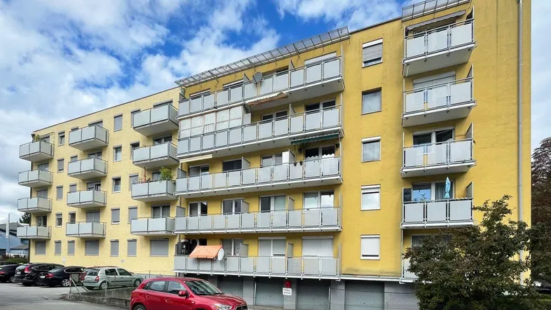 Gelbes Mehrfamilienhaus mit zahlreichen Balkonen und Außenparkplätzen unter blauem Himmel.