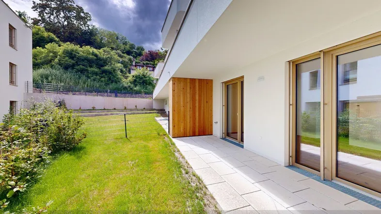 Moderne Wohnanlage mit privatem Gartenbereich und gepflasterter Terrasse, umgeben von grüner Landschaft.