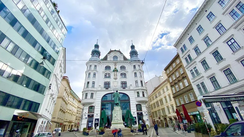 Historisches Gebäude an einer belebten Straße in der Stadt mit moderner Architektur im Hintergrund.