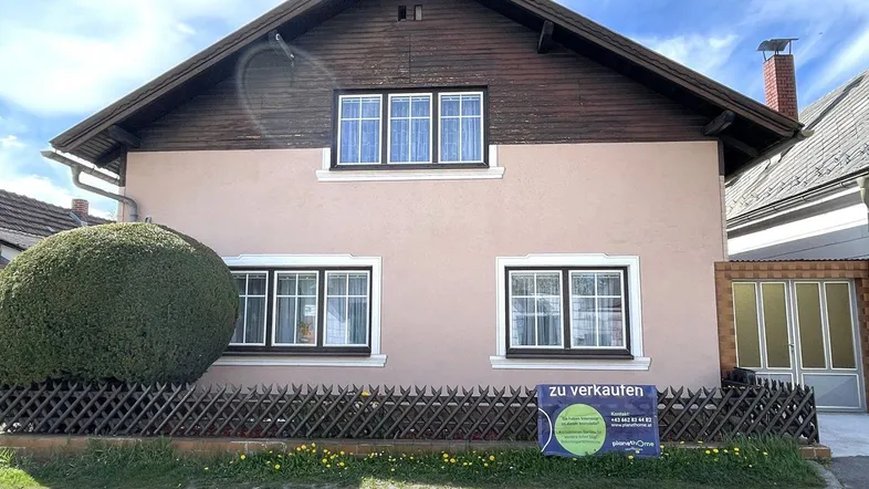 Vorderansicht eines Einfamilienhauses mit rosafarbener Fassade, Holzdachgiebel und kleinem Vorgarten.