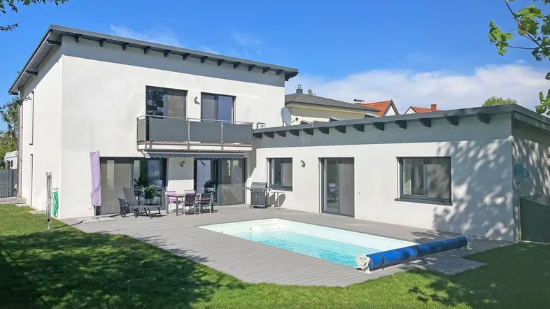 Moderne Villa mit Pool, Terrasse und Balkon, umgeben von einem gepflegten Garten.