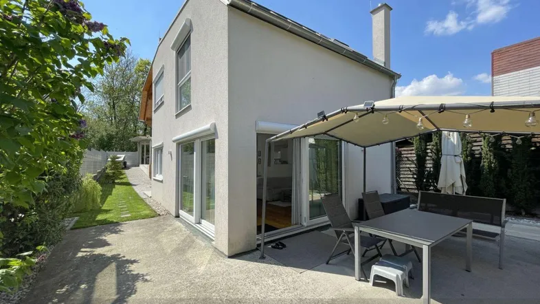 Moderne Hausfassade mit großer Terrasse und Gartenbereich unter einem Sonnensegel.