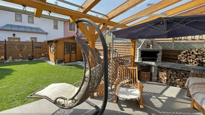 Gemütliche Terrasse mit Hängesessel, Grillplatz und Holzpergola, umgeben von einem gepflegten Garten.