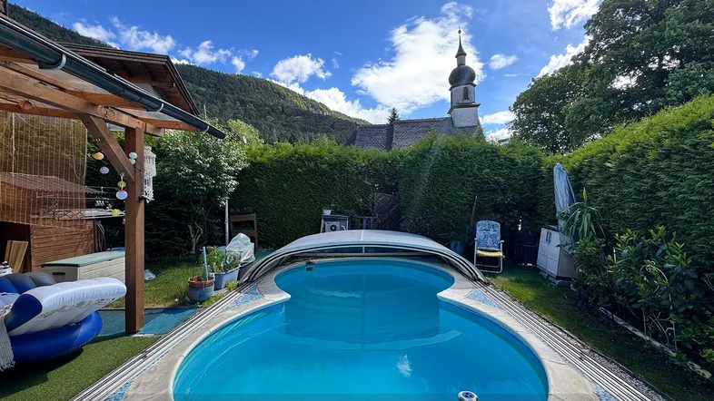 Großer Gartenbereich mit Pool und Blick auf die umliegende Berglandschaft und eine Kirche.