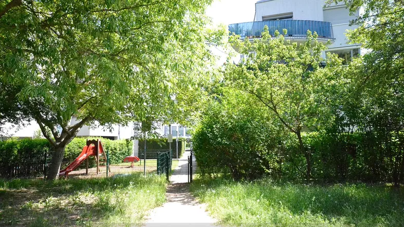 Grüner Außenbereich mit Spielplatz und modernem Wohngebäude im Hintergrund.