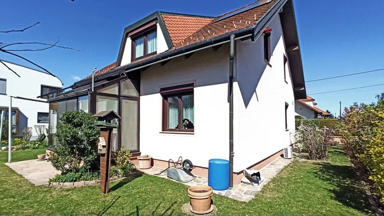 Seitlicher Blick auf das Einfamilienhaus mit Wintergarten, Garten und gepflegter Rasenfläche unter blauem Himmel.