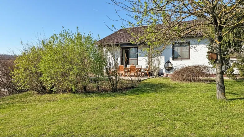 Sonnige Terrasse mit Gartenmöbeln und weitläufigem Rasenbereich vor einem gepflegten Einfamilienhaus.
