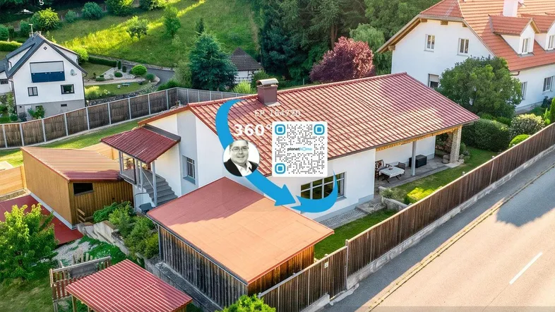 Luftaufnahme eines Einfamilienhauses mit rotem Dach, Garten und grüner Hügellandschaft im Hintergrund.