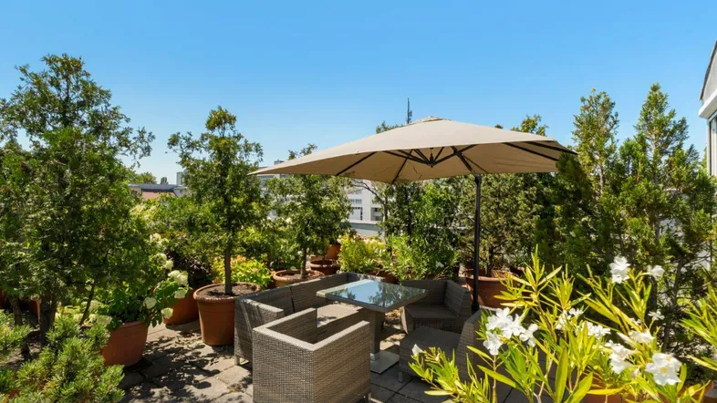 Möblierte Dachterrasse mit Sonnenschirm und vielen Pflanzen, ideal zum Entspannen im Freien.