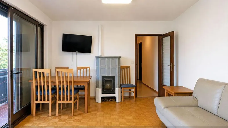 Heller Wohn-Essbereich mit Parkettboden, Kachelofen und Zugang zum Balkon.