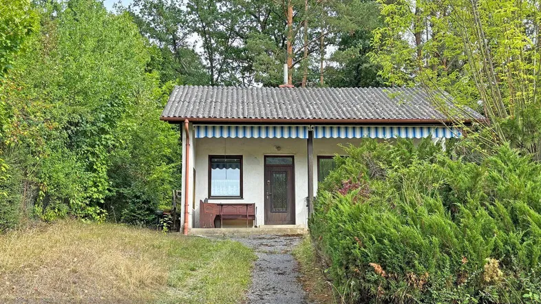 Kleines Haus umgeben von üppiger Vegetation und Bäumen in ländlicher Umgebung.