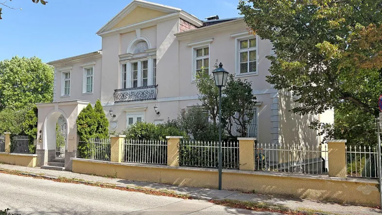 Elegante Villa mit klassischer Fassade und gepflegtem Vorgarten an einer ruhigen Straße.