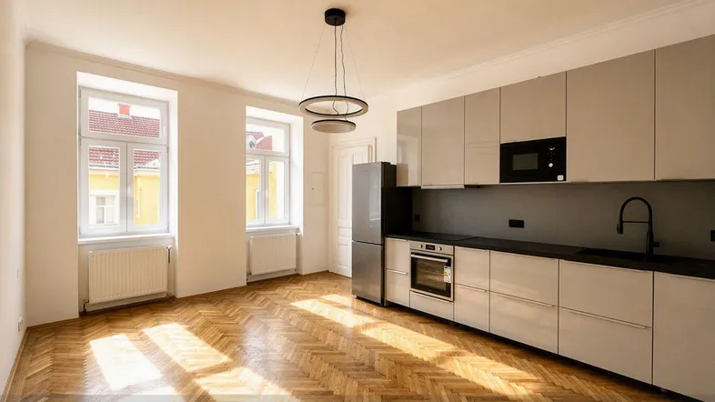 Moderne Küche mit hellgrauen Hochglanzfronten, dunkler Arbeitsplatte und Fischgrätparkettboden.