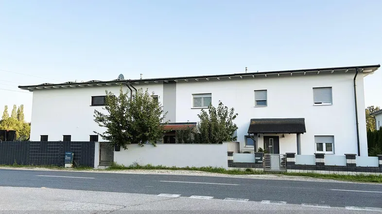 Weißes Mehrfamilienhaus mit moderner Fassade und gepflegtem Vorgarten an einer Straße.