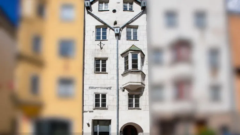 Schmales, traditionelles Gebäude mit weißer Fassade, mehreren Stockwerken und einem markanten Erker.