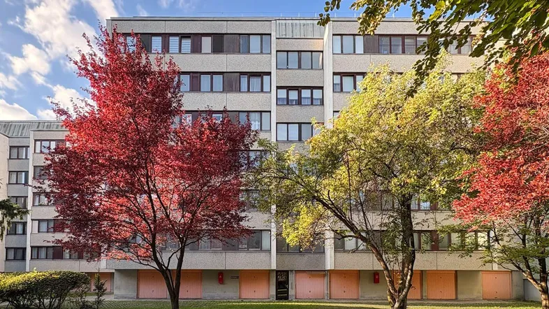 Mehrfamilienhaus mit mehreren Stockwerken und Bäumen in Herbstfarben vor der Fassade.