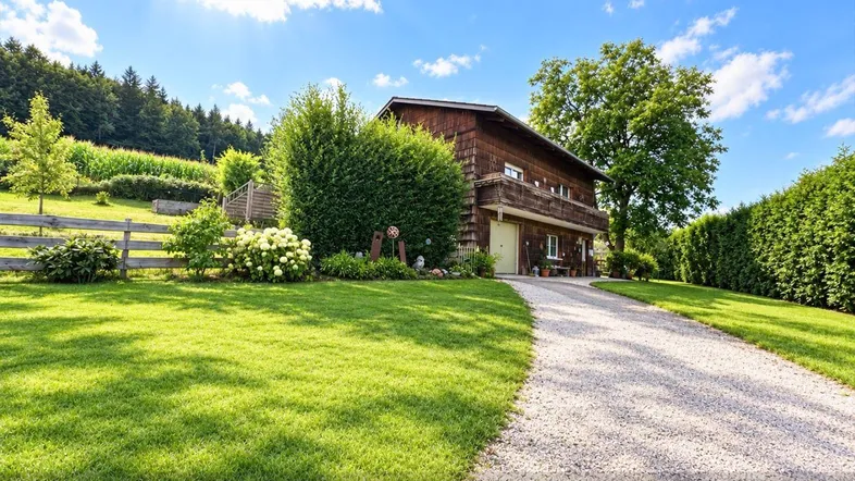 Charmantes Holzhaus mit gepflegtem Garten und sonniger Auffahrt in ländlicher Umgebung.