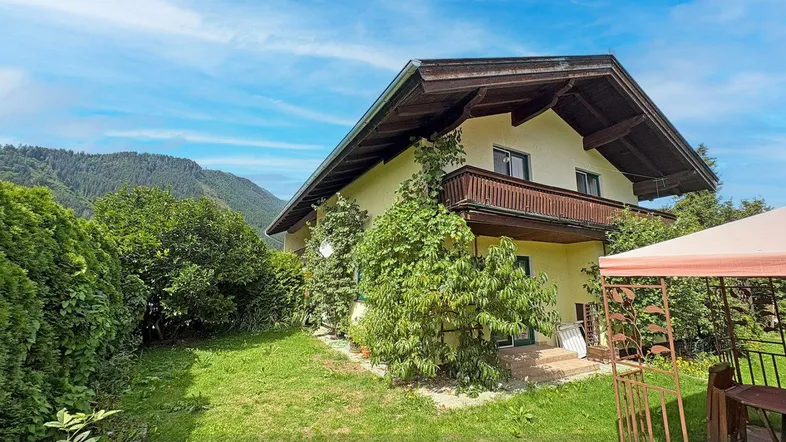 Traditionelles Haus mit großem Garten und Bergblick unter blauem Himmel.