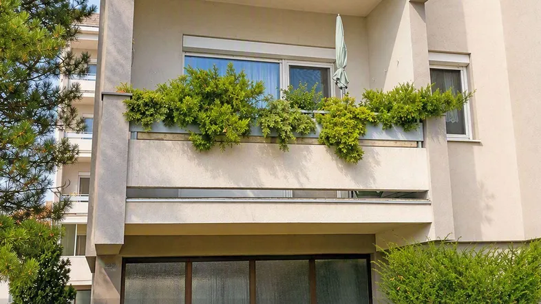 Balkon mit üppiger Bepflanzung und Sonnenschirm an der Fassade eines Mehrfamilienhauses.