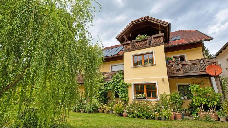 Gelbes Haus mit traditioneller Architektur, umgeben von einem gepflegten Garten und Bäumen.