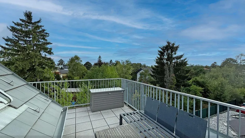 Geräumige Dachterrasse mit Sitzgelegenheiten und weitem Blick ins Grüne unter blauem Himmel.