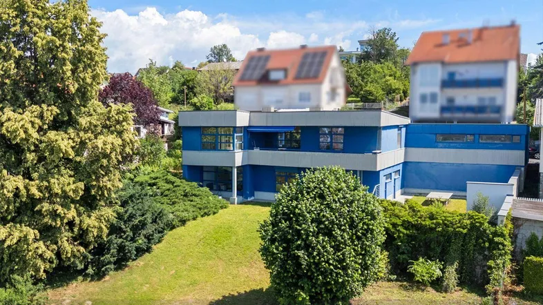 Modernes blaues Gebäude mit Flachdach und großem Gartenbereich unter blauem Himmel.