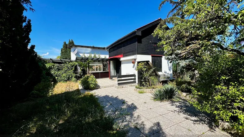 Hausfassade mit Gartenweg und üppigem Grün unter strahlend blauem Himmel.