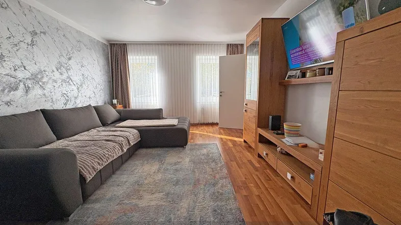 Helles Wohnzimmer mit großem Ecksofa, Holzboden und einer modern gestalteten Akzentwand.