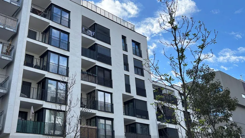 Moderne Wohnanlage mit weißer Fassade, großen Fenstern und Balkonen unter blauem Himmel.