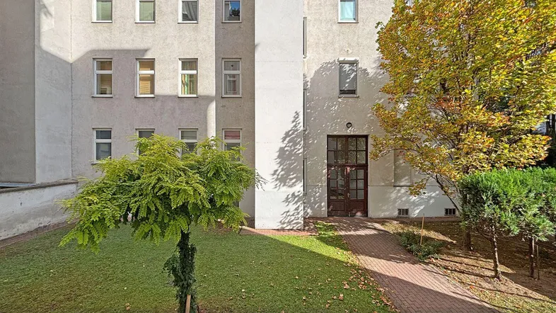 Außenansicht eines Mehrfamilienhauses mit gepflegtem Vorgarten und Bäumen im herbstlichen Laub.
