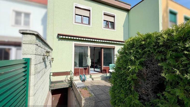 Rückseite des Hauses mit einer gepflasterten Terrasse, Markise und Zugang zum Keller.