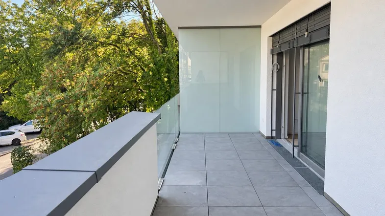 Geräumiger Balkon mit modernen Fliesen, Glasgeländer und Blick ins Grüne.