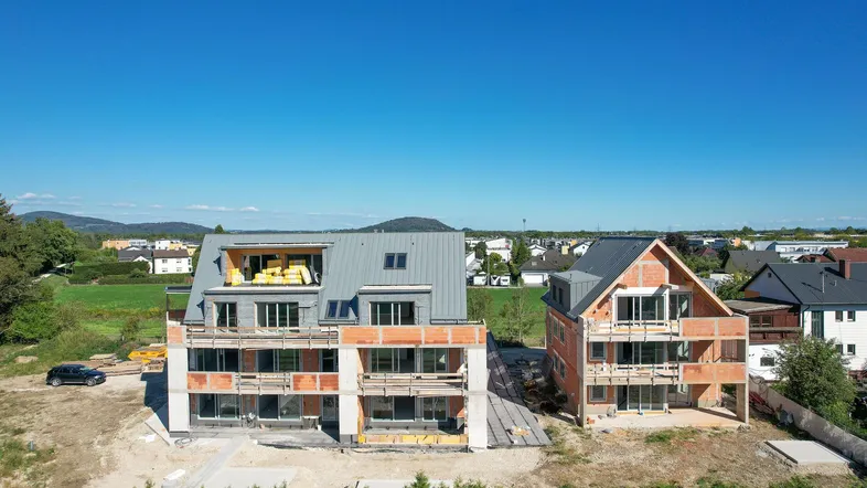 Luftaufnahme von zwei im Bau befindlichen Mehrfamilienhäusern mit Blick auf die umliegende Landschaft.