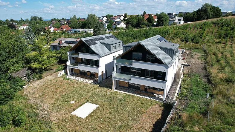 Luftaufnahme von zwei modernen, fertiggestellten Wohnhäusern mit Solaranlagen in grüner Umgebung.