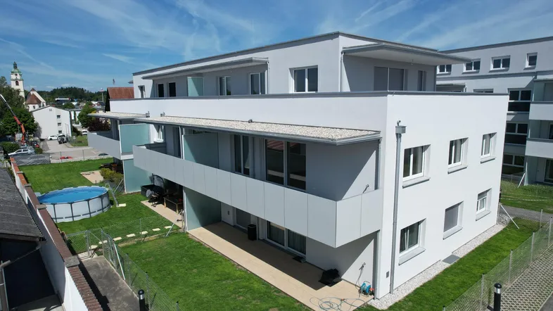 Moderne Wohnanlage mit Balkonen und einer ebenerdigen Terrasse, umgeben von einer gepflegten Grünfläche.