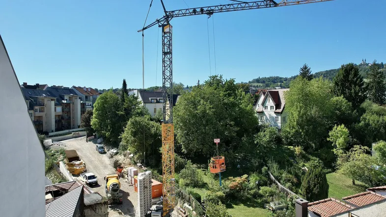 Baustelle mit großem Kran und umliegenden Wohngebäuden unter blauem Himmel.