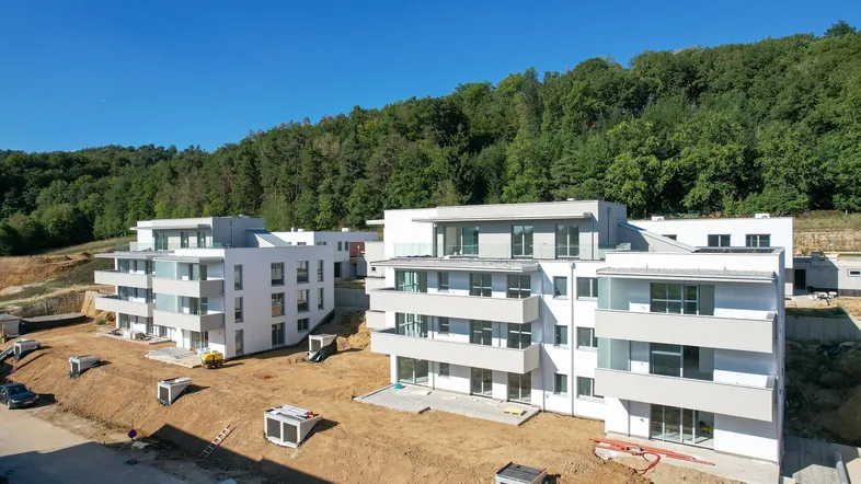 Luftaufnahme von modernen Neubauwohnungen im Bau, umgeben von grünen Hügeln und Wald.