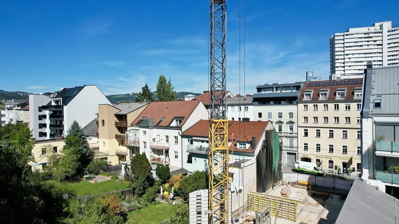 Baustelle mit Kran und umliegenden Wohngebäuden unter blauem Himmel.