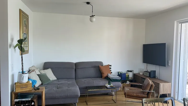 Helles Wohnzimmer mit modernem Sofa, Holzboden und Zugang zu einem Außenbereich.