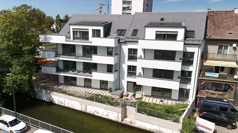 Modernes Mehrfamilienhaus mit weißer Fassade, Balkonen und Blick auf das Gewässer.
