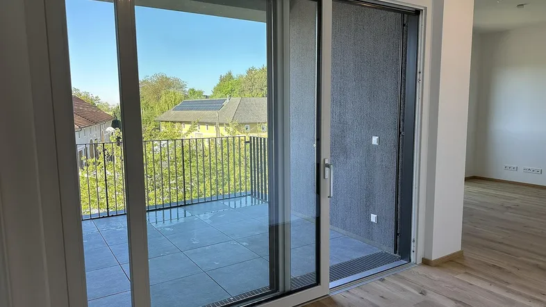 Heller Wohnbereich mit Schiebetür zum Balkon und Blick ins Grüne, ausgestattet mit Holzboden.