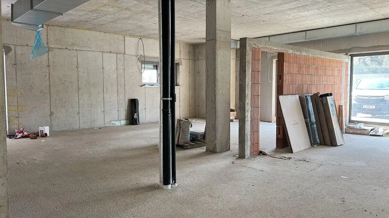 Großer Rohbau-Innenraum mit Betonwänden, freiliegenden Leitungen und Baustoffen, bereit für den Ausbau.