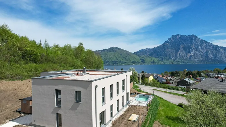 Modernes Gebäude mit Flachdach und kleinem Pool, umgeben von einer beeindruckenden Berg- und Seenlandschaft.