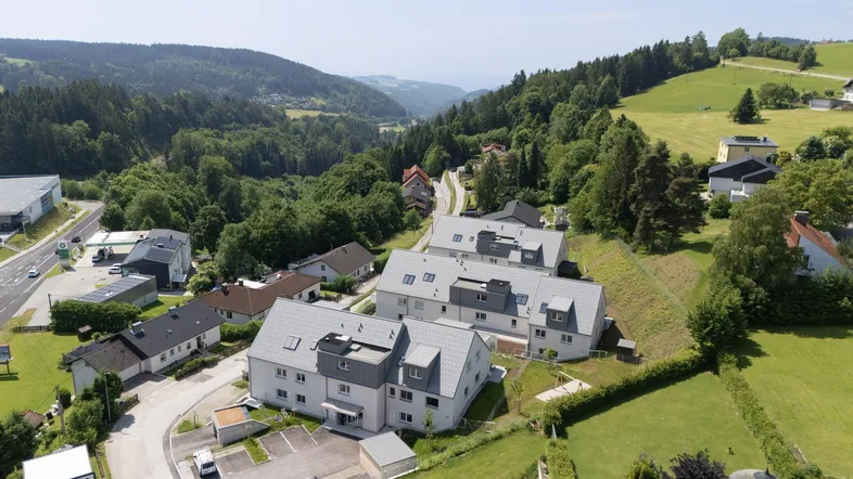 Panoramablick auf die Wohnanlage in einem grünen Tal, umgeben von Wäldern und Hügeln.