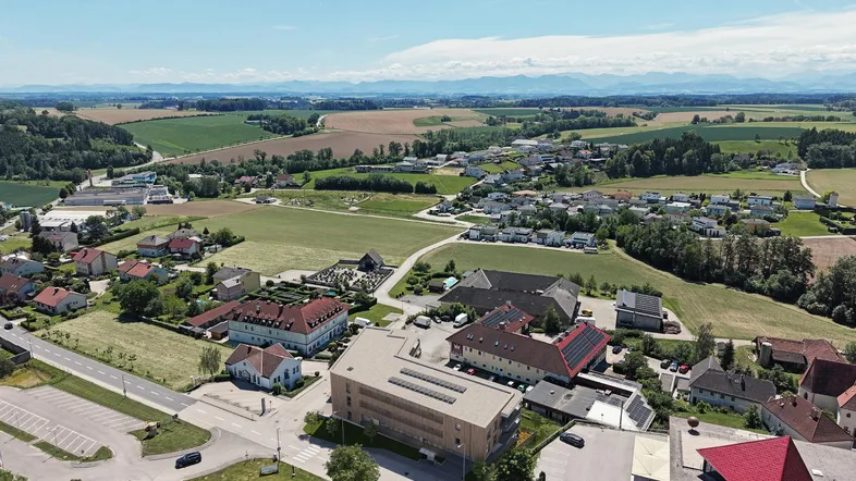 Luftaufnahme des Neubaus in ländlicher Umgebung mit Feldern und Bergen im Hintergrund.