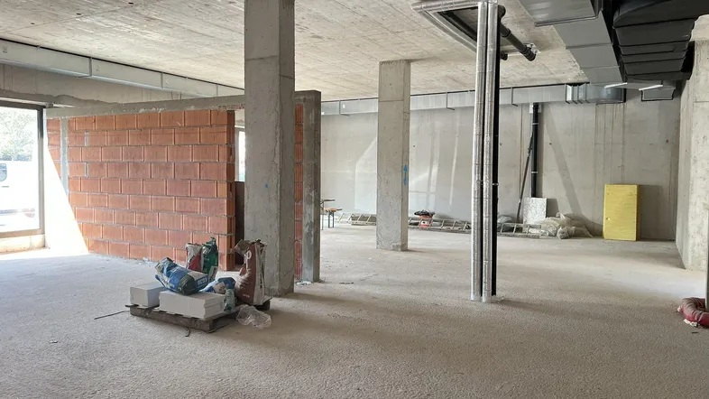 Unfertiger Innenraum mit Betonstützen, unverputzten Ziegelwänden und Baumaterialien auf dem Boden.